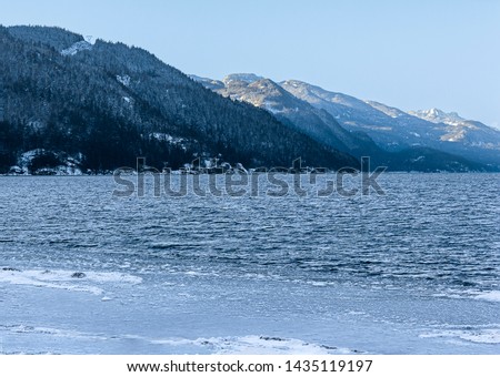 Beautiful winter landscape, snowy mountains at Harrison Hot Springs, British Columbia, Canada. Blue sky. Blue Harrison lake. Frozen ice on rocks in the foreground. Cold, freezing weather. Trees
