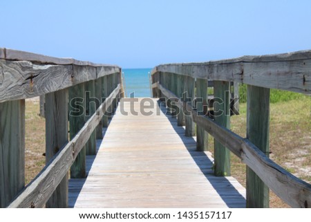 Perspective photograph of wooden walkover bridge to beach on sunny blue sky day with turquoise water and no clouds on the horizon.