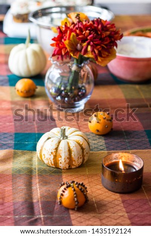 Pumpkins, oranges flowers and candles atop a seasonal tablecloth create a warm setting.