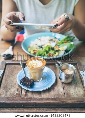 Woman's hands taking photo of coffee cup, Piccolo Latte, brownies with breakfast on wooden table by smartphone vertical style.