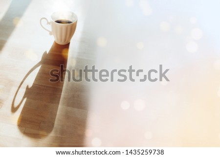 White cup with espresso standing on wooden table with long shadow side view. Breakfast tea with bokeh lights image. Good morning concept. Mug with hot drink, coffee beverage horizontal background