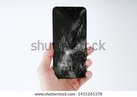 A man holds a smartphone in his hand with a broken screen on a white background