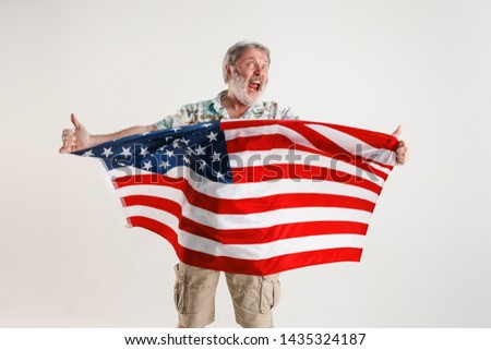 Celebrating an Independence day. Stars and Stripes. Senior man with the flag of the United States of America isolated on white studio background. Looks crazy happy and proud as a patriot of his