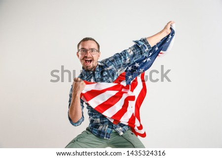 Celebrating an Independence day. Stars and Stripes. Young man with the flag of the United States of America isolated on white studio background. Looks crazy happy and proud as a patriot of his country