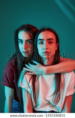 Unity of people. Studio shot indoors with neon light. Photo of two beautiful twins.