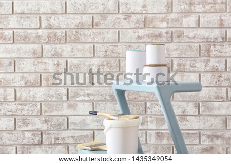 Cans of paint with supplies on step ladder near brick wall