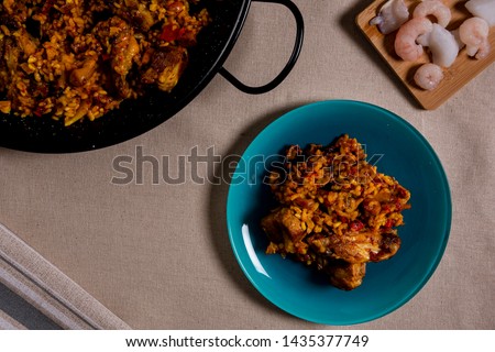 Overhead picture of rice with seafood and meat, on blue color dish, pan full of rice and raw seafood ingredients