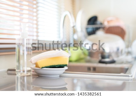 Yellow sponges and dish washing liquid soap on dirty sink fully with dishes and kitchen ware. Royalty-Free Stock Photo #1435382561