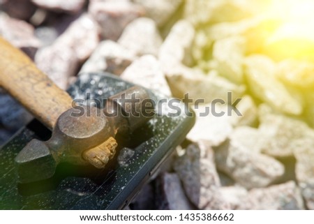 Broken glass of smartphone with hammer on gravel stones. Selective focus and sun beam lights.