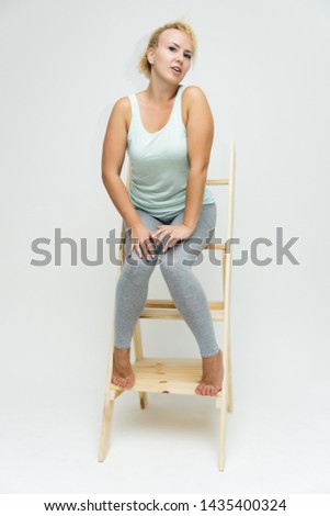 Full-length portrait of a slim beautiful pretty girl blonde woman with short curly hair on a white background in bright fitness clothes sitting on the stairs in various poses and a lot of emotions.
