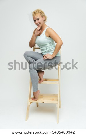 Full-length portrait of a slim beautiful pretty girl blonde woman with short curly hair on a white background in bright fitness clothes sitting on the stairs in various poses and a lot of emotions.