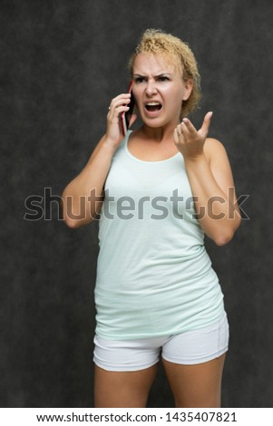 portrait above the knee of a beautiful blonde woman girl with short curly hair on a gray background in bright linen talking on the phone and showing a lot of emotions. Experienced model shows hands.