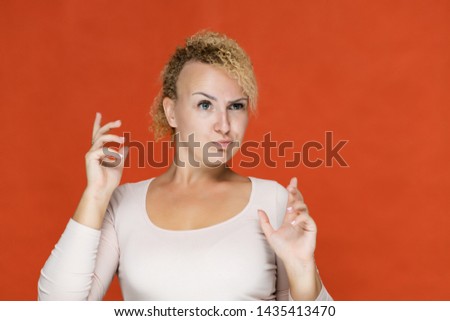 Photo portrait of a beautiful girl blonde woman with short curly hair on a red background talking and showing a lot of emotions. An experienced model shows hands. Beauty. Made in studio