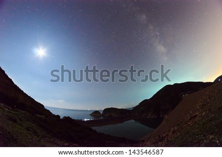 A picture of the moon and the milkyway galaxy with a dam of High Island Reservoir, Hong Kong Global Geopark in the foreground. Contain Noise.