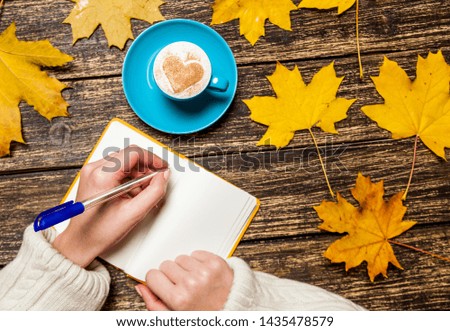 Female hand writing something in notebook near cup of coffee.