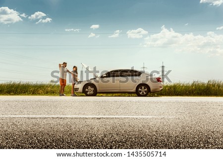 The young couple broke down the car while traveling on the way to rest. They are trying to fix the broken by their own or should hitchhike, getting nervous. Relationship, troubles on the road Royalty-Free Stock Photo #1435505714