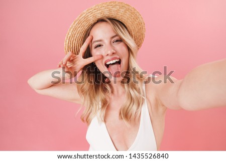 Happy pretty young girl wearing swimsuit standing isolated over pink background, taking a selfie, showing peace gesture