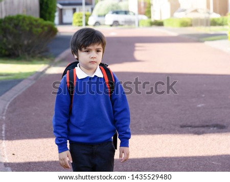 Portrait of Child with bored face holding plastic toy and carrying backpack waiting for school bus, Unhappy Pupil of primary school looking down with sad face standing alone, Kid back to school