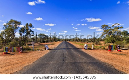 Entry gate with cattle grid across the bitumen road leading to Lightning ridge opal mine town away from Highway in outback NSW of Australia.