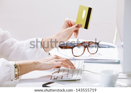 Young woman making payments online while typing on the computer / Young businesswoman with a credit card on hand.
