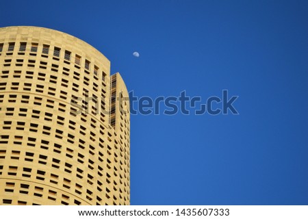 Downtown round building with half moon in blue sky.
