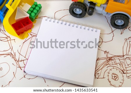 Notepad with white sheets surrounded by toy dump truck and tractor with colored plastic cubes on the background illustration with tractors. Grunge style. Mockup. Copy space. Top view 