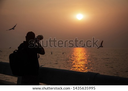 silhouette photographer take sunset photo at dock and seascape with camera