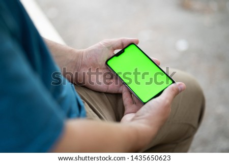 close up handsome man use left hand typing mobile phones and touch screen working with app devices in park with sunrise and green blur nature background.