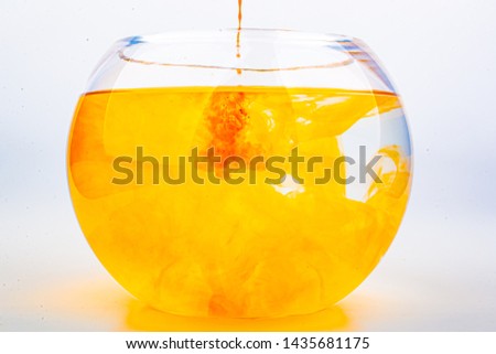 Orange food coloring diffuse in water inside round bowl glass with empty copyspace area for slogan or advertising text message, over isolated white background.