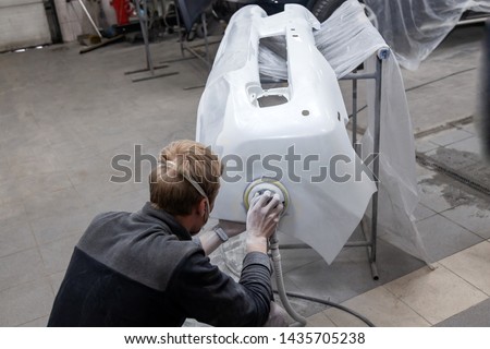 Preparation for painting a car element using sander and putty by a service technician leveling out before applying a primer after damage to a part of the body in an accident in the vehicle workshop Royalty-Free Stock Photo #1435705238