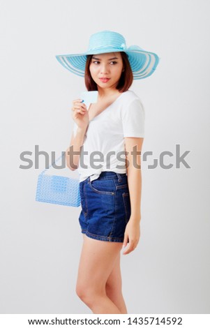 Young beautiful asian woman black hair in hat hand holding credit card and bag standing against white background for making payment
