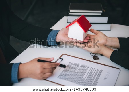 Real estate agent holding house model to customer finised signing contract papers in office. Business successful contract concept.