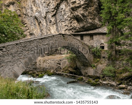 small river in the mountains, slow shutter speed for smooth water level and dreamy effect, arched bridge, Alps