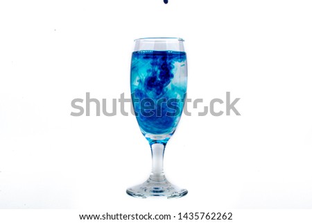 Blue food coloring diffuse in water inside wine glass with empty copyspace area for slogan or advertising text message, over isolated white background.