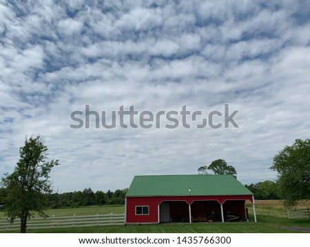Red barn with Green Roof in a grassy field with blue sky and small trees around. Short grass with leading lines, lean-to and white fence. Small planes visible in some pictures. Summer day.