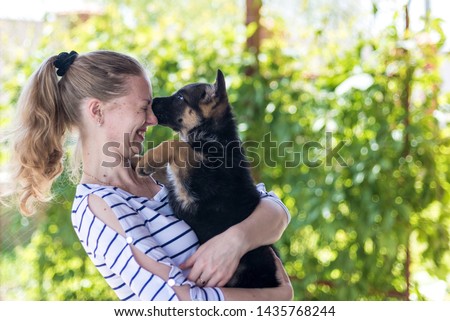 Portrait. Happy girl holding a small puppy German shepherd and smiles. Purchase and purchase of a dog, the joy of the first meeting with the animal. On a green blurred background with copy space