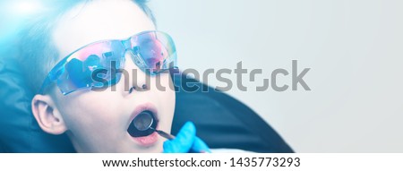 The boy with goggles in the dental chair. The doctor examines the oral cavity with a special dental mirror