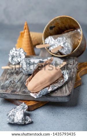 Artisanal ice cream on a stick wrapped in silver foil on a wooden serving board, selective focus.