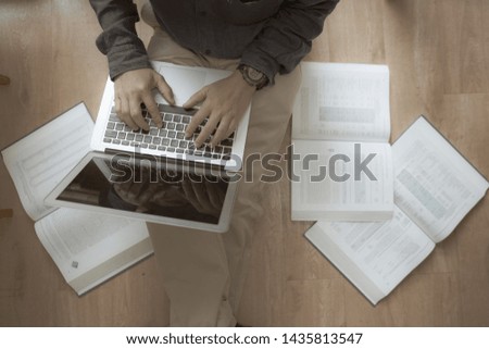 Asian man sitting on floor and working on laptop with books around 