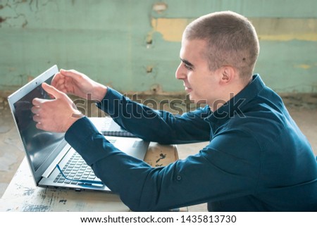 Photo of a student in blue shirt with a laptop in front of him, preparing for the exam.  Talking to a laptop. Difficulty in learning, education concept