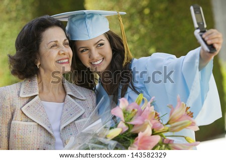 Female graduate and grandmother taking picture with cellphone outside