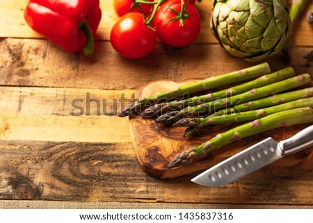 Asparagus, and an artichoke, a sprig of tomatoes and sweet red peppers on a cutting board with a knife, sliced. on a wooden background. a culinary background. horizontal photo