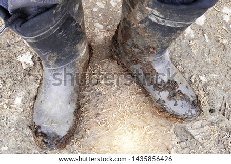 Top view of legs in black dark dirty rubber boots or wellingtons in mud and clay and manure