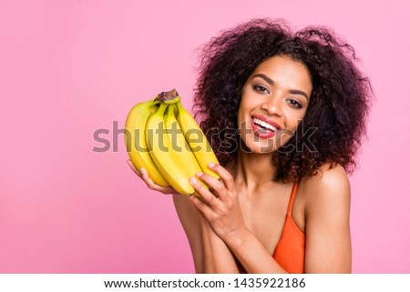 Close up photo beautiful funny she her dark bronze skin body model lady hold hands arms exotic fruit bananas toothy beaming smile fresh food eat wear swimming orange suit isolated pink background
