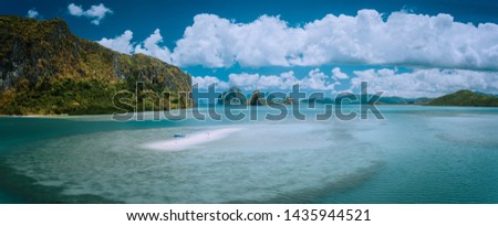 Palawan, Philippines. Aerial panoramic scenic picture of sandbar with lonely tourist boat in turquoise coastal water and cloudscape. El Nido Bacuit archipelago. Many limestone Island in background