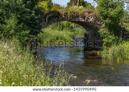 An old stone bridge, overgrown with grass, crosses the stream. Summer Sunny day.
