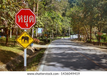 Elephant crosswalk symbol at the road for warning people who through this way.Yellow sign is elephant cross walk and another red one in Thai language is "STOP" sign.