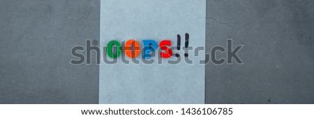 The multicolored oops word is made of wooden letters on a grey plastered wall background.