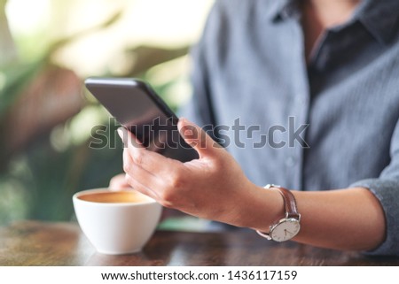 Closeup image of a woman holding  and using mobile phone with coffee cup on wooden table in cafe