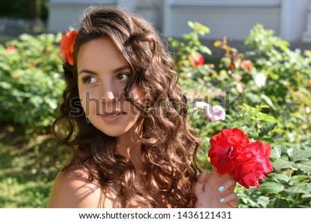 young beautiful girl with curls next to red roses in the garden